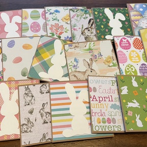 May include: A collection of handmade Easter cards featuring a variety of colorful patterns and a white bunny silhouette. The cards are made with brown cardstock and have a rustic, handmade look.