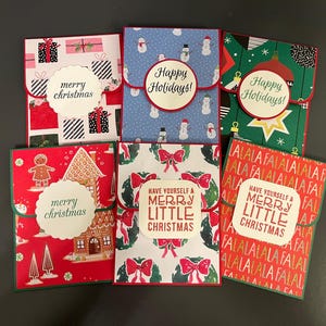 May include: Six different Christmas card designs with red, green, and white colors. The cards feature various holiday themes, including gingerbread houses, snowmen, and wreaths. The cards have different messages, including "Merry Christmas", "Happy Holidays", and "Have Yourself a Merry Little Christmas".