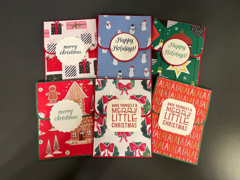 May include: Six different Christmas card designs with red, green, and white colors. The cards feature various holiday themes, including gingerbread houses, snowmen, and wreaths. The cards have different messages, including "Merry Christmas", "Happy Holidays", and "Have Yourself a Merry Little Christmas".