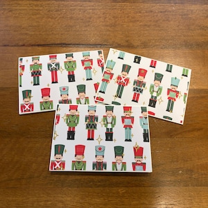 May include: Three rectangular cards with a repeating pattern of toy soldiers in red, green, and blue uniforms on a white background. The cards are arranged on a wooden surface.
