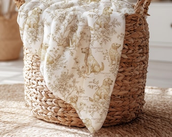 Puede incluir: Una manta blanca con un patrón repetitivo estilo toile en color beige, que representa perros golden retriever sentados entre arreglos florales y follaje. El texto Harrison James está impreso en una fuente cursiva junto a cada ilustración.