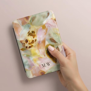 May include: A rectangular e-reader case featuring a glossy, abstract watercolor pattern in shades of soft pink, sage green, yellow, and brown. The bottom center of the case displays the black serif initials M|W printed in a clean, vertical line format.