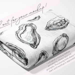 May include: Folded white blanket with a black and white oyster illustration. The blanket has a repeating pattern of oyster shells. The text "Look out for your mockup!" is written in cursive. The blanket is folded on a white surface.