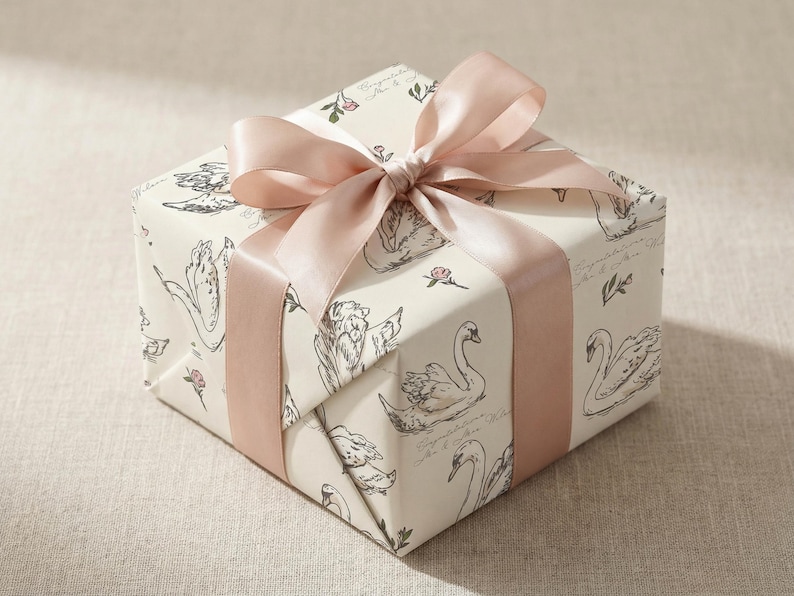 Blush pink satin ribbon tied around a gift box wrapped in personalized swan wedding wrapping paper with soft ivory background delicate floral details and romantic bridal shower styling