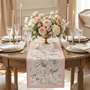May include: A beautifully set dining table with a floral centerpiece, candles, and place settings. The table features a floral runner with a pink border. The setting includes gold-toned cutlery, crystal glasses, and pink napkins.