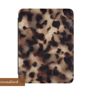 May include: A rectangular protective case for an electronic reader featuring a tortoiseshell pattern with dark brown and black spots on a cream background. The bottom left corner displays a brown rectangular label with the text Not Personalized.