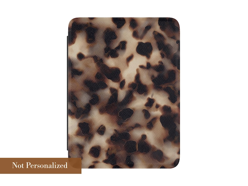 May include: A rectangular protective case for an electronic reader featuring a tortoiseshell pattern with dark brown and black spots on a cream background. The bottom left corner displays a brown rectangular label with the text Not Personalized.