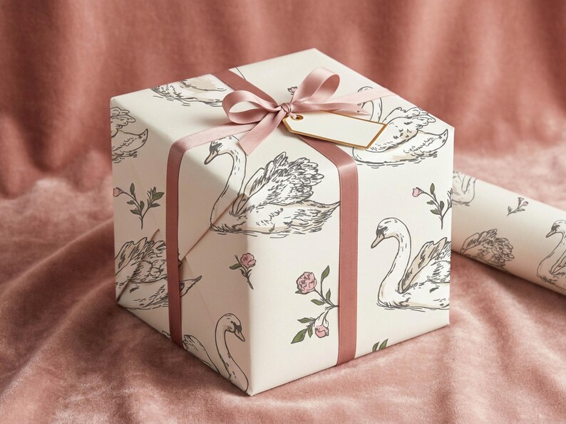 Gift box wrapped in romantic swan wedding paper with blush satin ribbon and blank tag styled on pink velvet for feminine bridal shower gift wrap presentation