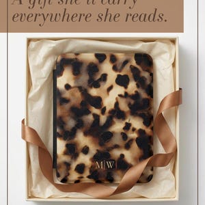 May include: A rectangular e-reader case featuring a brown and black tortoiseshell pattern with the gold-coloured initials M|W centred at the bottom. The case is presented inside a square box lined with cream-coloured tissue paper and a brown ribbon.