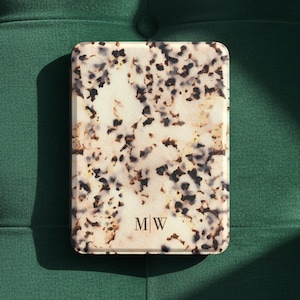 May include: A rectangular e-reader case featuring a cream-colored base with a mottled tortoiseshell pattern in shades of brown and black. The lower center of the case displays the gold-colored monogram letters M and W separated by a vertical line.
