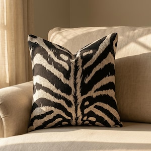 May include: A square throw pillow featuring a bold, high-contrast zebra stripe pattern in black and off-white. The fabric displays a textured, woven appearance with organic, irregular lines radiating from the center of the cushion cover.