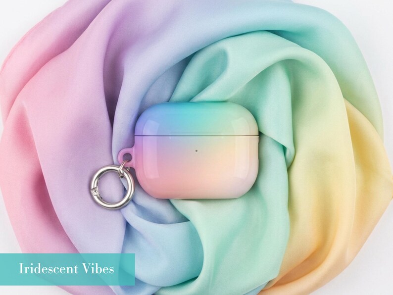 May include: A protective case for wireless earbuds featuring a smooth, gradient finish that transitions from soft pink to yellow, green, and blue. The case includes a silver-toned metal ring attachment on the side and displays the text Iridescent Vibes.