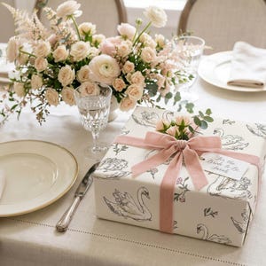 Wedding table setting with floral centerpiece and blush ribbon gift wrapped in swan bridal shower wrapping paper styled as elegant bride present packaging