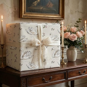 Large gift wrapped in swan wedding wrapping paper displayed on an antique wood table with candles roses and lace ribbon for romantic bridal shower wedding decor inspiration