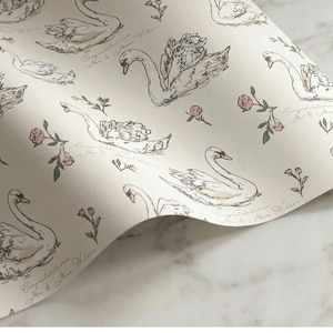 Detailed closeup of swan wrapping paper pattern with ivory background blush floral accents and personalized congratulations text for wedding bridal shower gift presentation