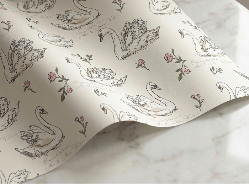 Detailed closeup of swan wrapping paper pattern with ivory background blush floral accents and personalized congratulations text for wedding bridal shower gift presentation