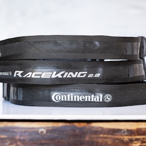 Op de afbeelding: Drie zwarte fietsbanden met het Continental-logo en de tekst "RaceKing 2.2" in wit.