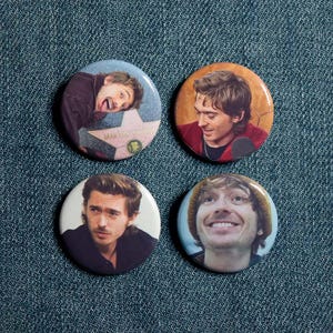 May include: Four circular pinback buttons featuring photographic portraits of the same person. One button shows a person near a Hollywood star, another shows a person in a red shirt, one shows a person in a black shirt, and one shows a person wearing a beanie.