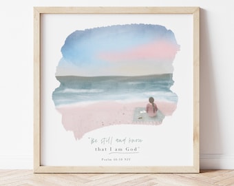 May include: A watercolour painting of a woman sitting on a beach with a book. The sky is a soft pink and blue, and the sea is a deep blue. The text "Be still and know that I am God" is written below the image, along with the verse "Psalm 46:10 NIV".