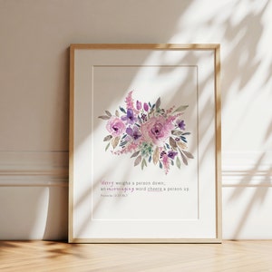 May include: A framed print with a watercolor painting of a bouquet of pink and purple flowers. The print includes the text "Worry weighs a person down, an encouraging word cheers a person up. Proverbs 12:25 NLT."