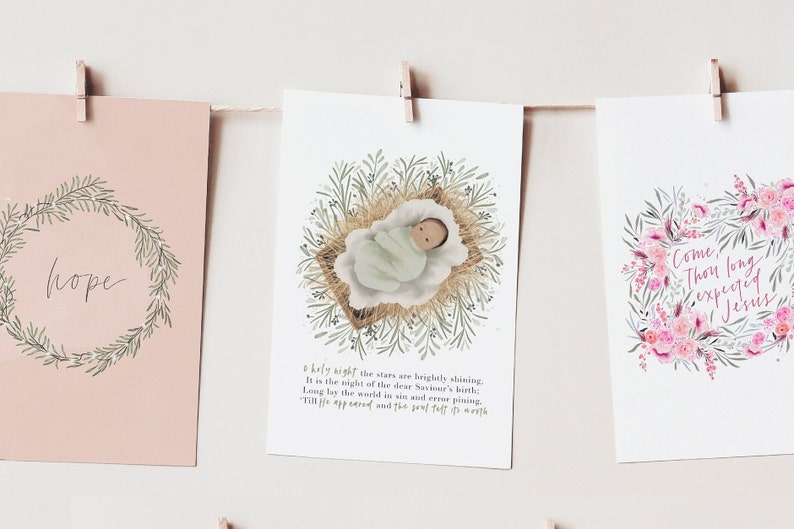 May include: Three printable Christmas cards with watercolor illustrations. The first card features a wreath with the word "hope" in the center. The second card features a baby in a manger with a green and brown floral wreath around it. The third card features a pink and green floral wreath with the text "Come, Thou long expected Jesus".