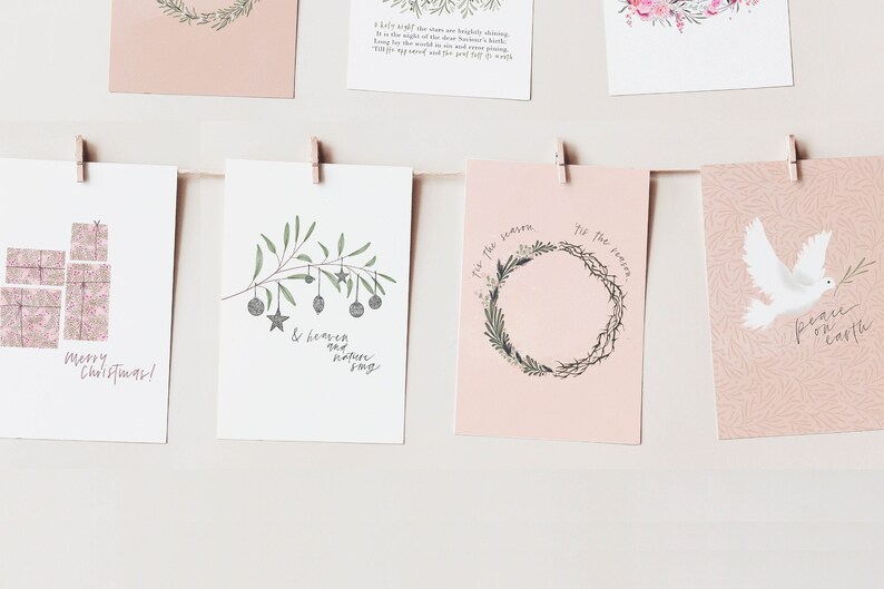 May include: Five Christmas cards with pink backgrounds and various illustrations. The cards feature a stack of presents, a branch with ornaments, a wreath, a dove with an olive branch, and a text-based card that reads "Peace on Earth".