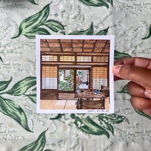 May include: Watercolour painting depicting a traditional Japanese interior with a garden view. The room has wooden beams, paper screens, and a table with dishes. The painting is signed "Kyoto, 22.04.25".
