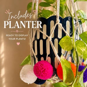 May include: A macrame plant hanger made of off-white cord holding a dark blue and white scalloped planter with a green pothos plant. The hanger features white, hot pink, orange, and purple pom-poms. Text reads: Includes PLANTER READY TO DISPLAY YOUR PLANTS!