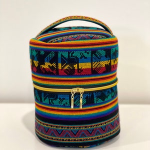May include: A cylindrical, black, zippered, fabric bag with a handle. The bag is decorated with colorful stripes and geometric patterns in shades of red, yellow, blue, green, and black.