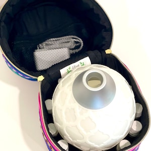 May include: A round, white essential oil diffuser with a silver top sits inside a colorful, striped zippered carrying case. The case has a black lining and a mesh pocket. The diffuser is surrounded by small, clear glass bottles.