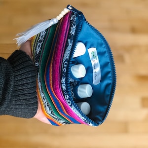 May include: A blue zippered pouch with a colorful striped pattern and a white tassel. The pouch is open and contains several small white bottles with a label that reads "A Mark of Love".