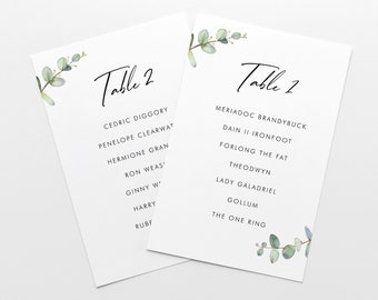 May include: Two white cards with green eucalyptus leaves and black text. The top card says "Table 2" and lists names like Cedric Diggory, Penelope Clearwater, Hermione Gran, Ron Weas', Ginny W', Harry, and Rubf. The bottom card says "Table 1" and lists names like Meriadoc Brandybuck, Dain II Ironfoot, Forlong the Fat, Theodwyn, Lady Galadriel, Gollum, and The One Ring.