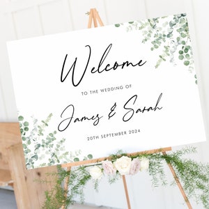 May include: White wedding welcome sign with green eucalyptus leaves and the text "Welcome to the wedding of James & Sarah 20th September 2024".