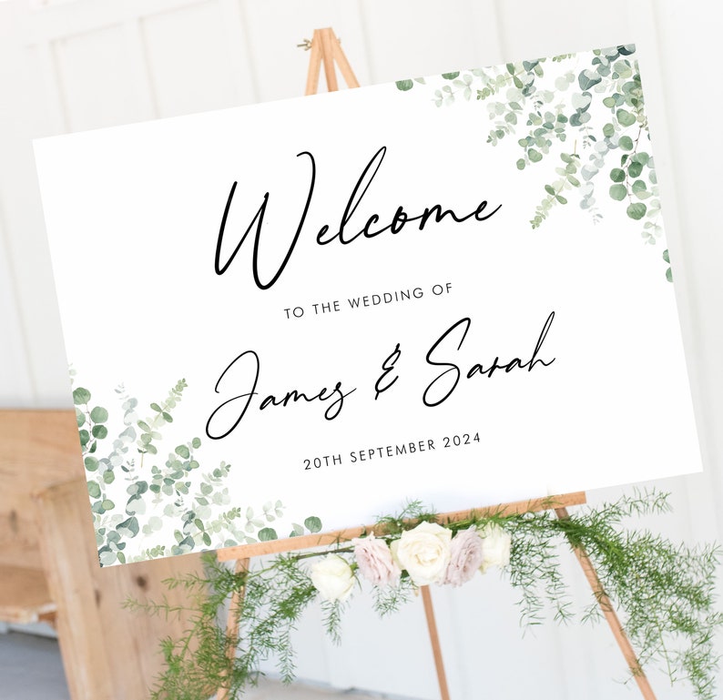 May include: White wedding welcome sign with green eucalyptus leaves and the text "Welcome to the wedding of James & Sarah 20th September 2024".