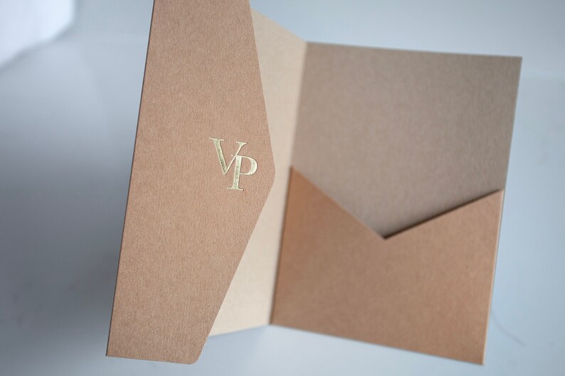 May include: A tan presentation folder with a pocket, featuring a gold foil stamped "VP" monogram. The folder is open, revealing a lighter tan interior. The paper has a textured finish.