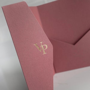 May include: Dusty rose-colored stationery set with a textured finish. The set includes a folded card and an envelope. The initials "VP" are embossed in gold on the front of the card. The stationery is displayed on a white surface.