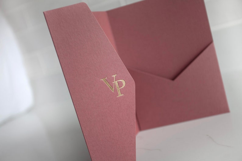 May include: Dusty rose-colored stationery set with a textured finish. The set includes a folded card and an envelope. The initials "VP" are embossed in gold on the front of the card. The stationery is displayed on a white surface.