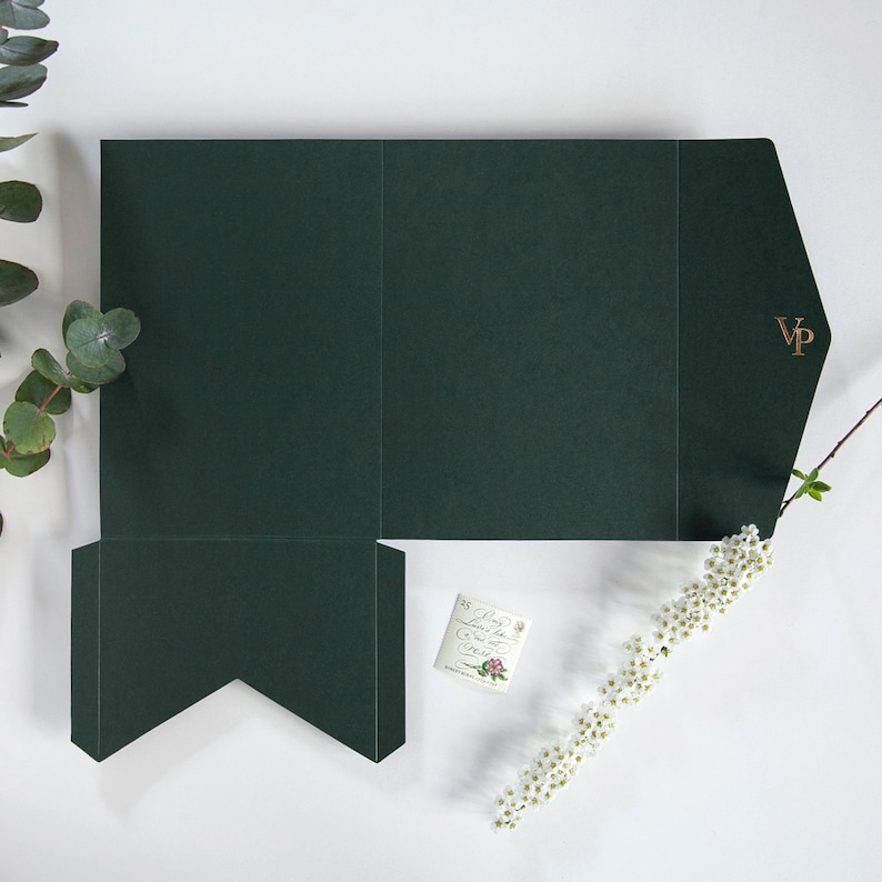 May include: Dark green folded presentation box with a gold foil "VP" monogram. The box is open and flat, with a small card and sprigs of white flowers and eucalyptus leaves. The box is designed for packaging.