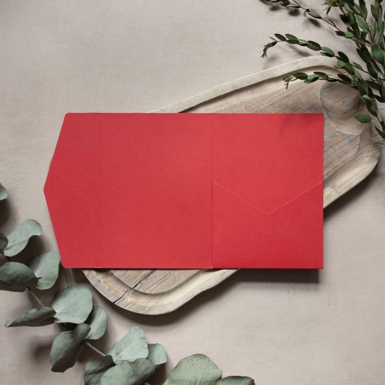 May include: A red envelope with a flap on the left side. The envelope is lying on a wooden surface.