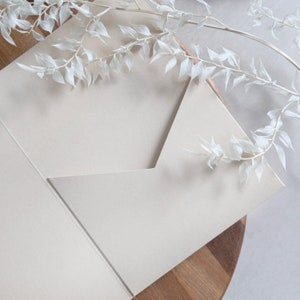 Puede incluir: Un sobre blanco con una solapa doblada, que se encuentra sobre una superficie de madera. Ramas blancas secas con hojas est&aacute;n dispuestas sobre el sobre.