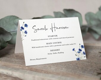 May include: A white folded menu card featuring blue cornflower illustrations on the left and right sides. The text reads Sarah Harrison, STARTER Traditional minestrone with croutons and shaved parmesan, MAIN COURSE Wild mushroom risotto, DESSERT Sticky Toffee Pudding, and Dietary Requirements.