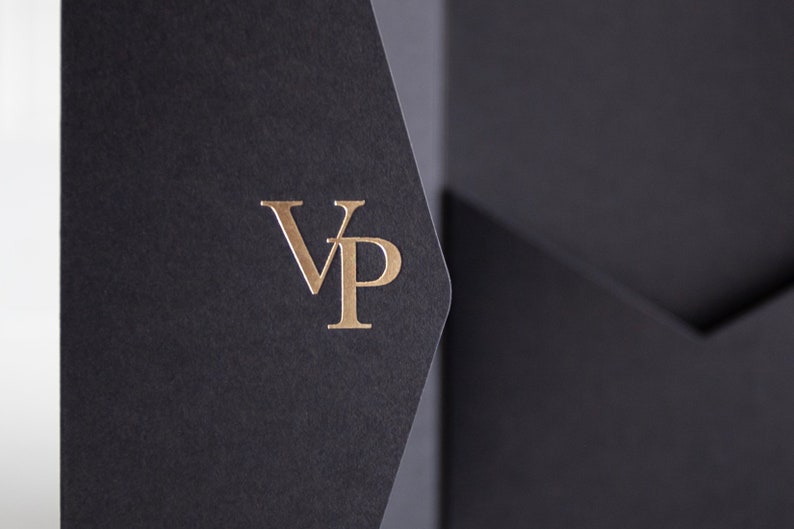 May include: Close-up of a black presentation folder with a gold foil stamped "VP" logo. The folder is made of textured paper and has a pocket. The background is a soft, neutral color.