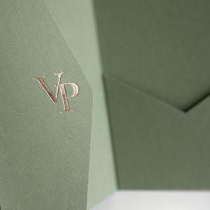 May include: Sage green stationery with a gold foil "VP" monogram. The paper has a textured finish and is folded to create a pocket. The design is simple and elegant, suitable for invitations or announcements.