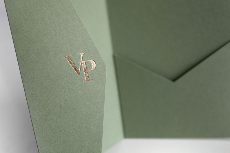 May include: Sage green stationery with a gold foil "VP" monogram. The paper has a textured finish and is folded to create a pocket. The design is simple and elegant, suitable for invitations or announcements.