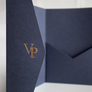 May include: Navy blue presentation folder with a gold foil "VP" monogram. The folder is open, revealing a pocket on the right side. The paper has a textured finish, and the background is white.