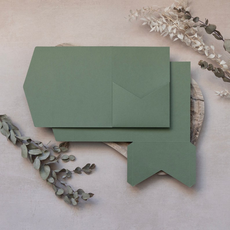 May include: A set of three green paper envelopes with a pocket on the front. The envelopes are folded and stacked on a wooden surface.