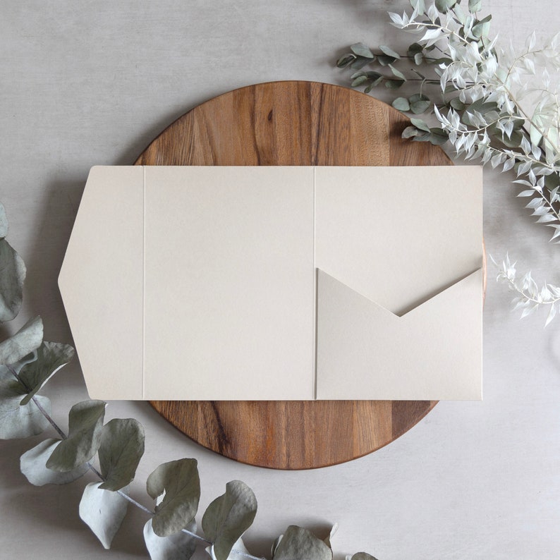 Puede incluir: Una tarjeta blanca con una solapa plegable, sentada sobre una superficie de madera. La tarjeta est&aacute; en blanco y lista para escribir.