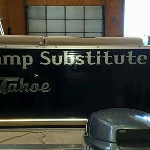 K&ouml;nnte beinhalten: Ein schwarzes Pontonboot mit dem Text "Camp Substitute Tahoe" in silbernen Buchstaben auf der R&uuml;ckseite.