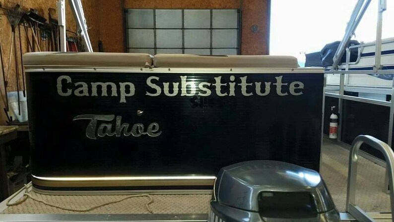 K&ouml;nnte beinhalten: Ein schwarzes Pontonboot mit dem Text "Camp Substitute Tahoe" in silbernen Buchstaben auf der R&uuml;ckseite.