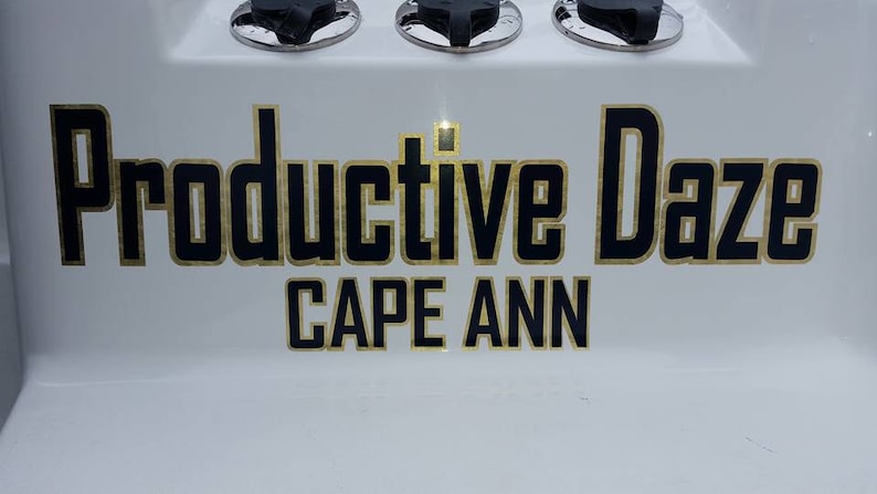 K&ouml;nnte beinhalten: Ein wei&szlig;es Schild mit schwarzem Text, der "Productive Daze" mit goldener Umrandung lautet. Unter dem Text steht "CAPE ANN" in goldenen Buchstaben.